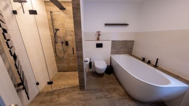 Badewanne mit schwarzer 3-Loch-Armatur, Toilette und Dusche mit Pendeltür
